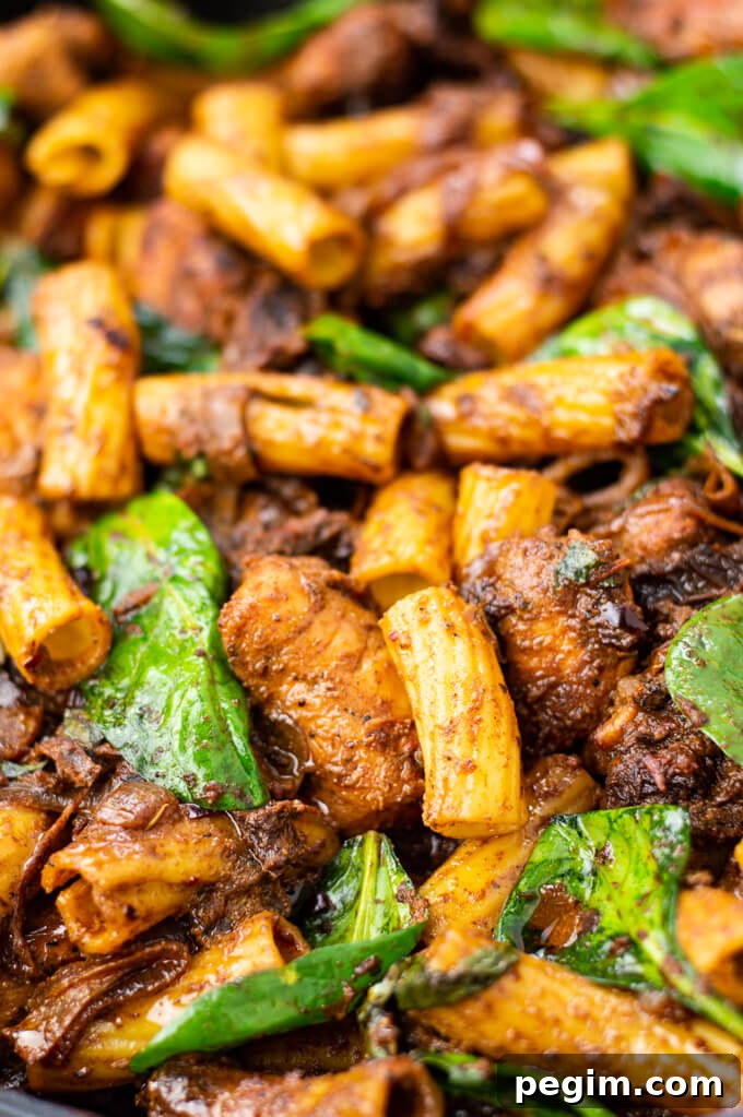 A close-up photo of chicken pasta with sun-dried tomatoes and spinach.
