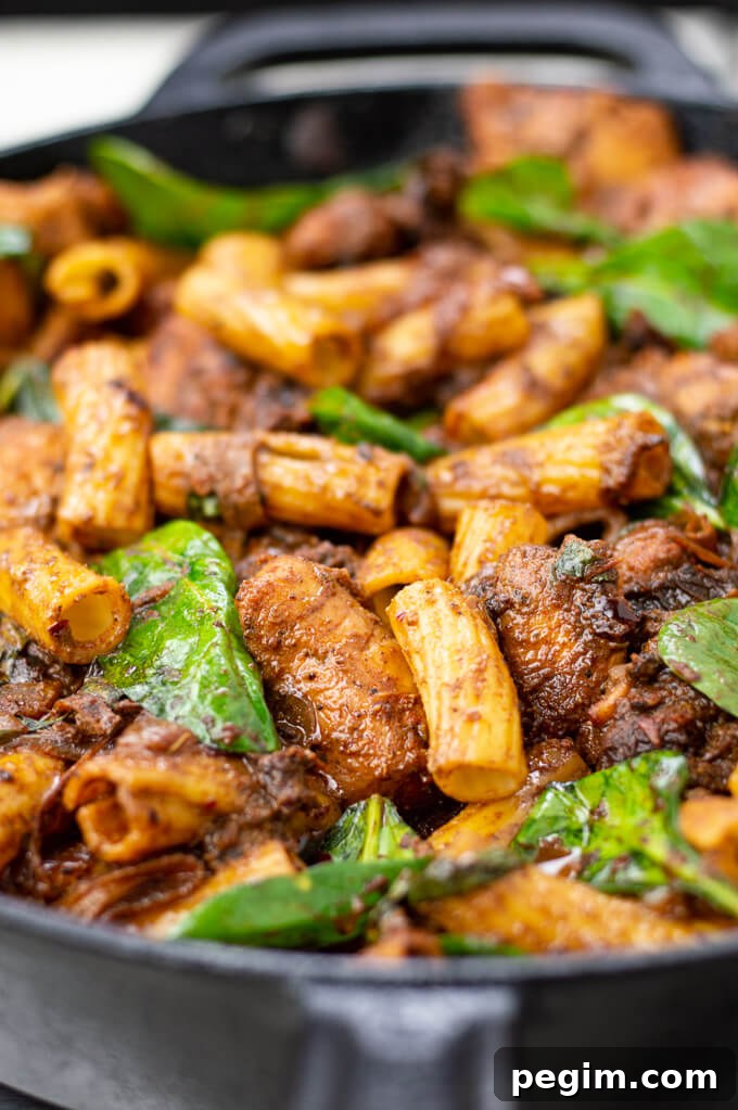 A cast iron skillet of chicken pasta with sun-dried tomatoes and spinach.