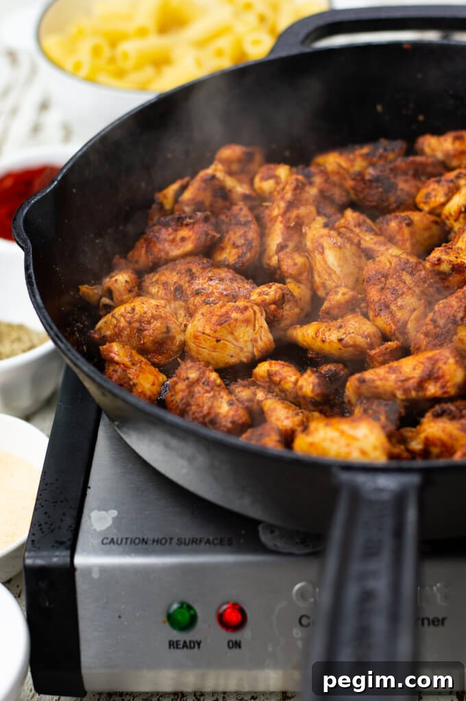 A black cast iron skillet with cooked chicken tender cubes rubbed with spices.