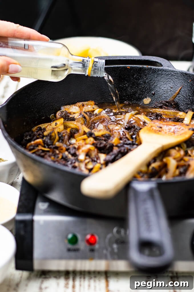 White wine is being poured into a skillet of sauteed onions and sun-dried tomatoes.