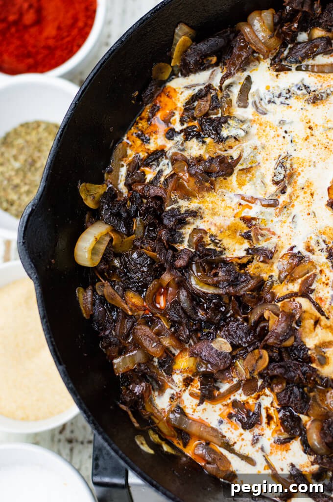 A black cast iron skillet with saute onions, sun-dried tomatoes and cream.