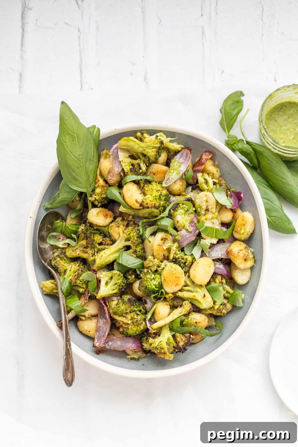 Sheet pan pesto gnocchi in a serving dish with a basil garnish.