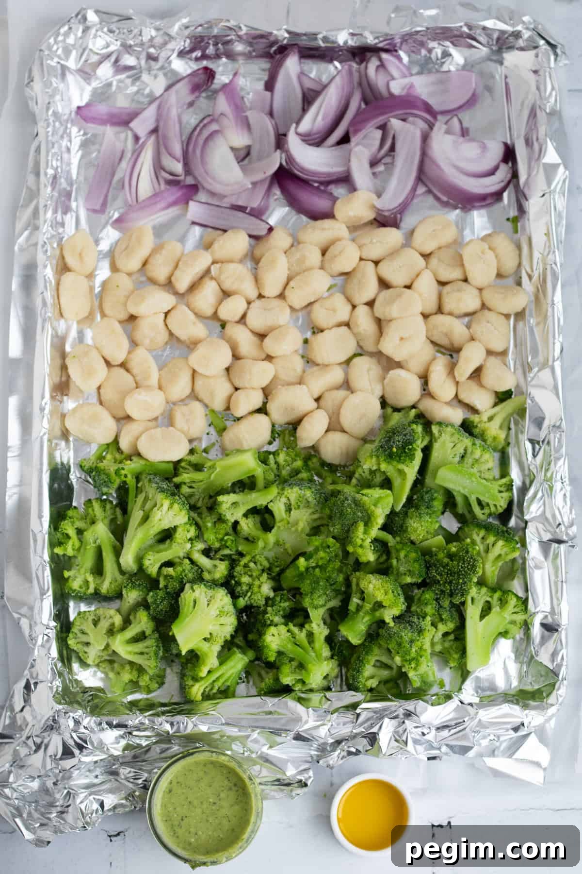 red onion, gnocchi, broccoli, pesto and oil on a sheet pan.
