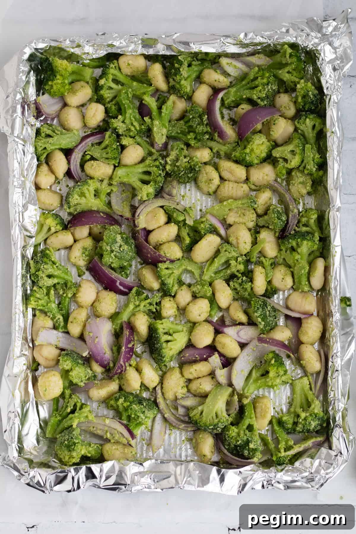 gnocchi, vegetables and pesto spread out on a sheet pan.