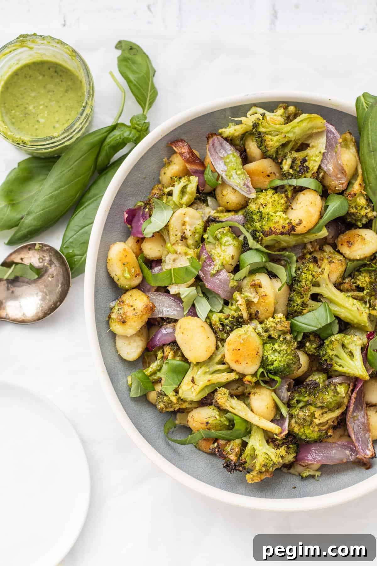 Sheet pan gnocchi with pesto in a serving dish with a basil and pesto on the side