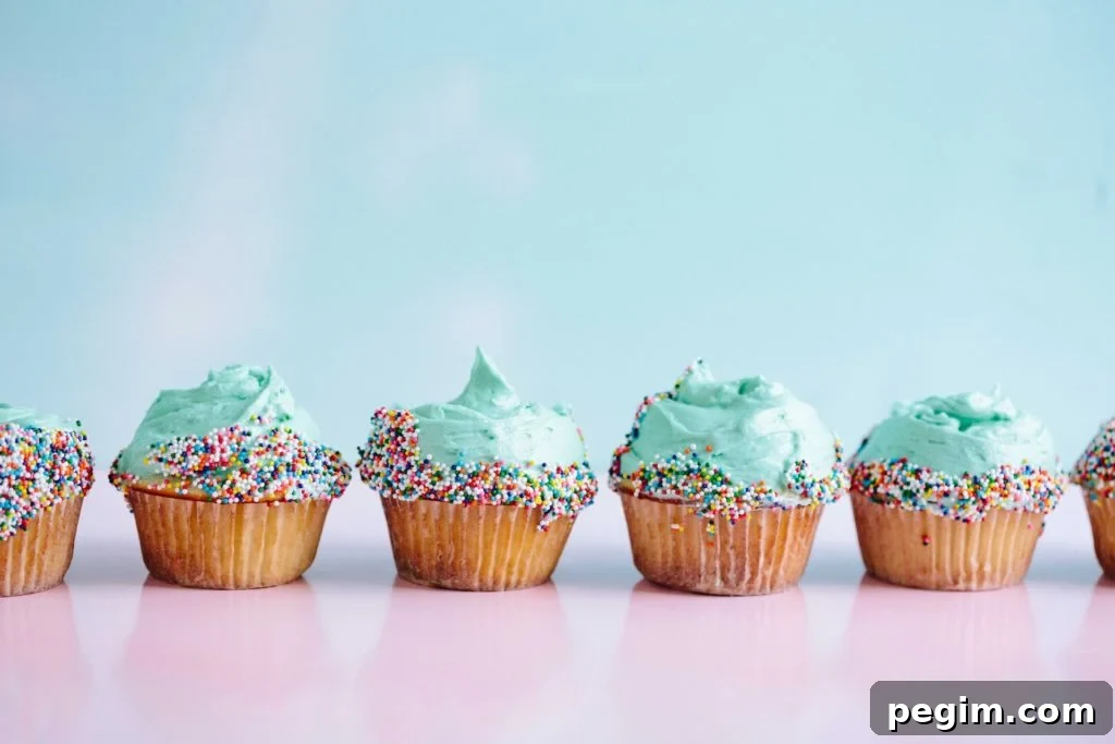 six cupcakes with teal frosting and sprinkles lined up on a pink countertop. 