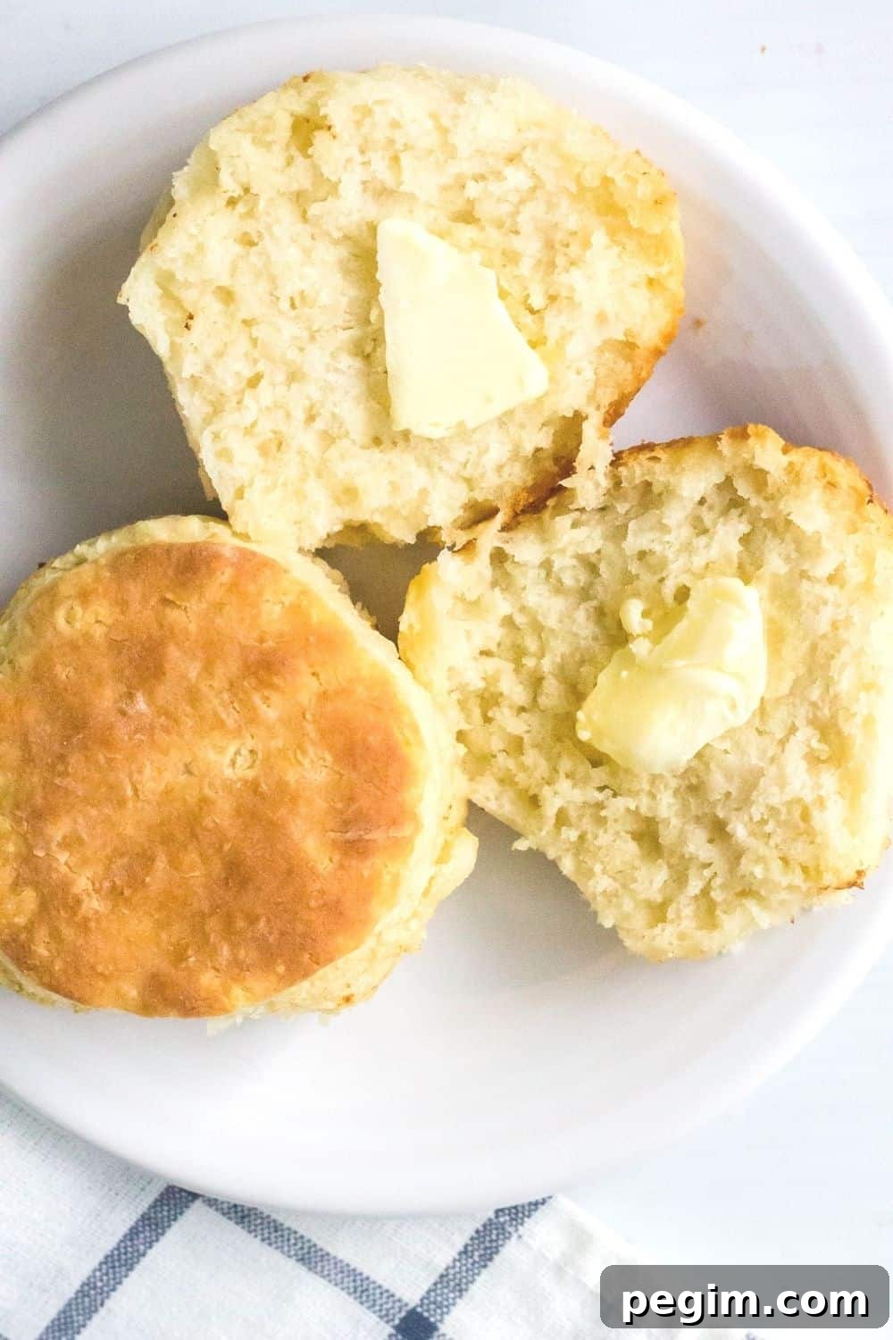 two easy homemade biscuits on a white plate, with one biscuit split open and buttered.