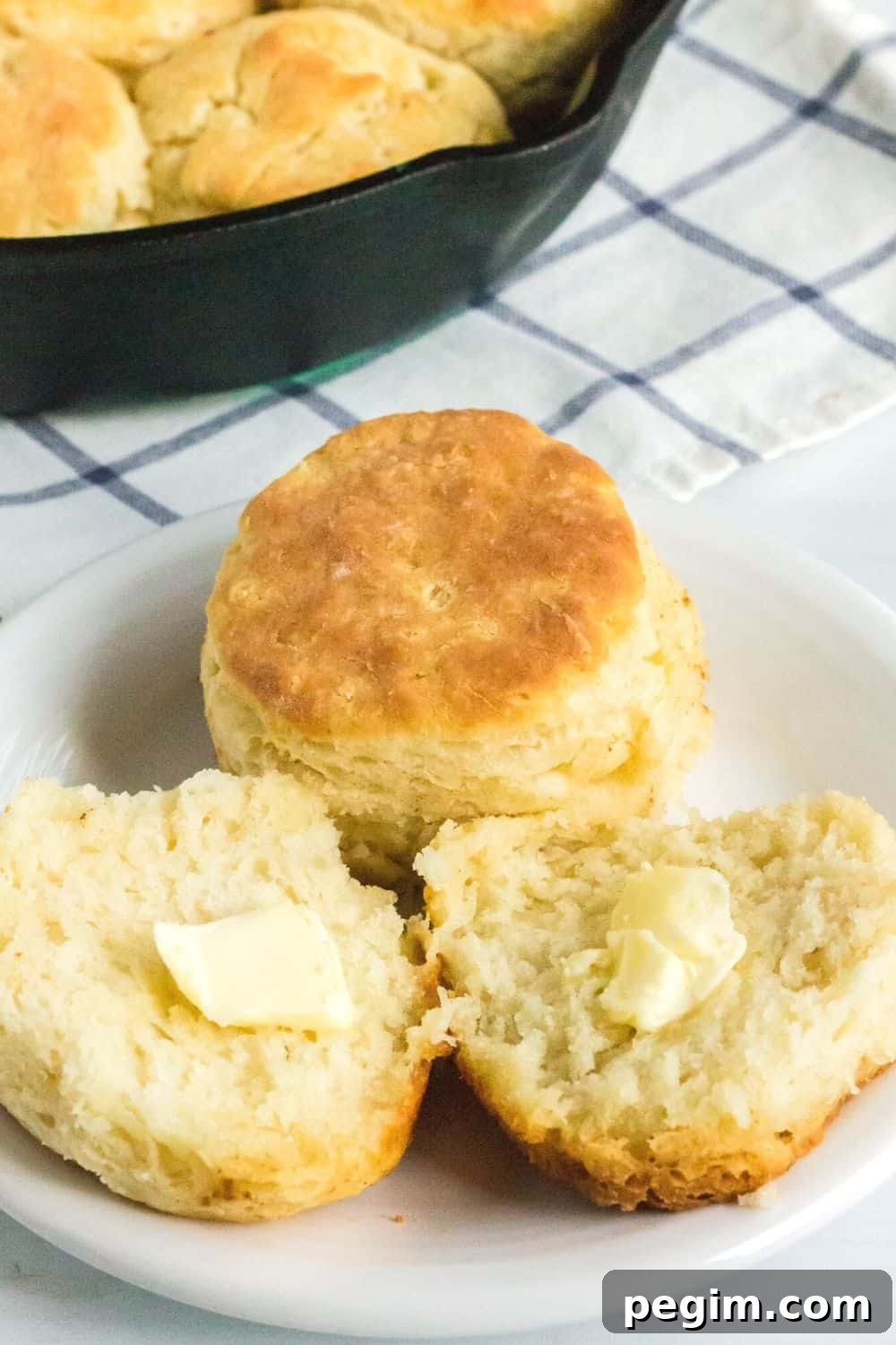 a split biscuit, topped with butter, along with a whole biscuit on a white plate