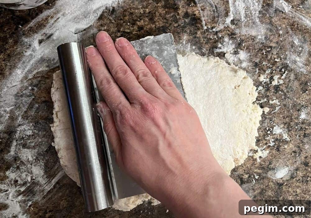 A woman's hand presses on a bench scraper to flatten biscuit dough into a 1-inch disk.