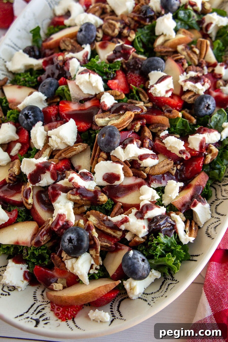 a large platter with a kale salad topped with berries, peaches, nuts, and balsamic vinaigrette.