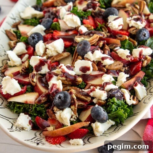 a white bowl with salad made with kale, fruit, nuts, and cheese.