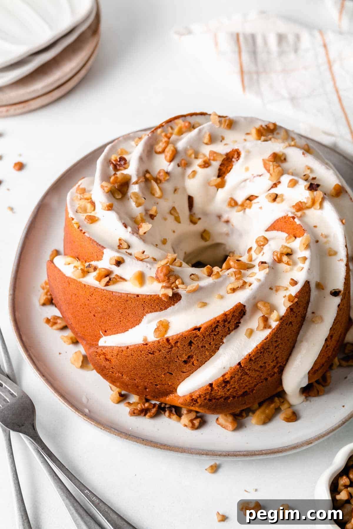 Gluten-free pumpkin bundt cake on a plate with white cream cheese icing dripping down the sides, sprinkled with chopped walnuts. 