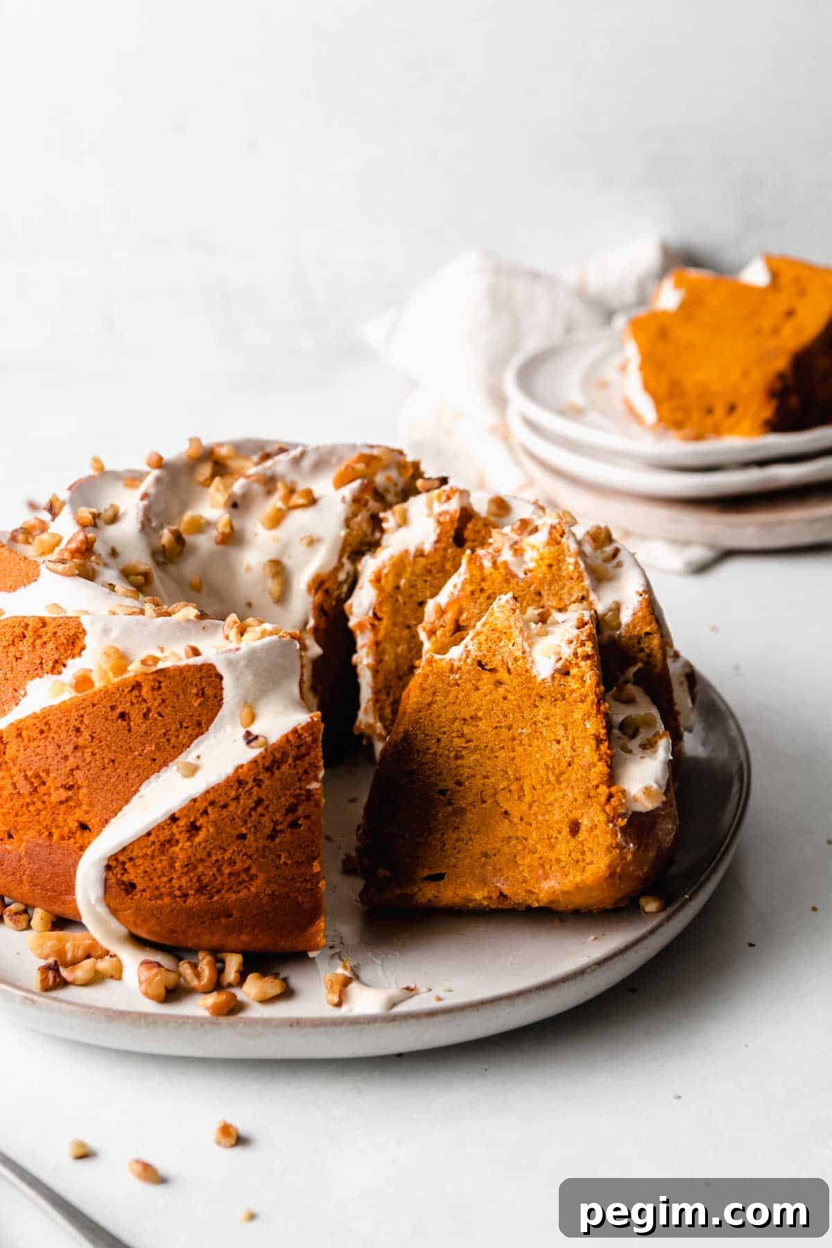 Partially sliced pumpkin bundt cake is orange with white icing, slices rest against the rest of the unsliced cake.