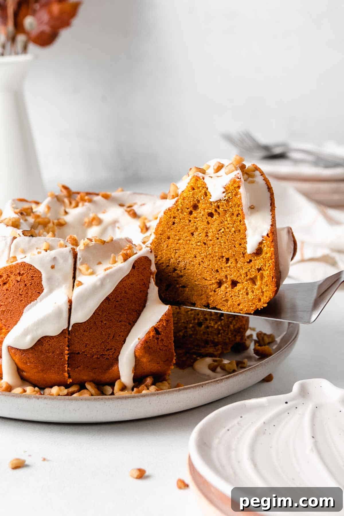 A slice of pumpkin cake is on a serving spatula as it is lifted from the cake.