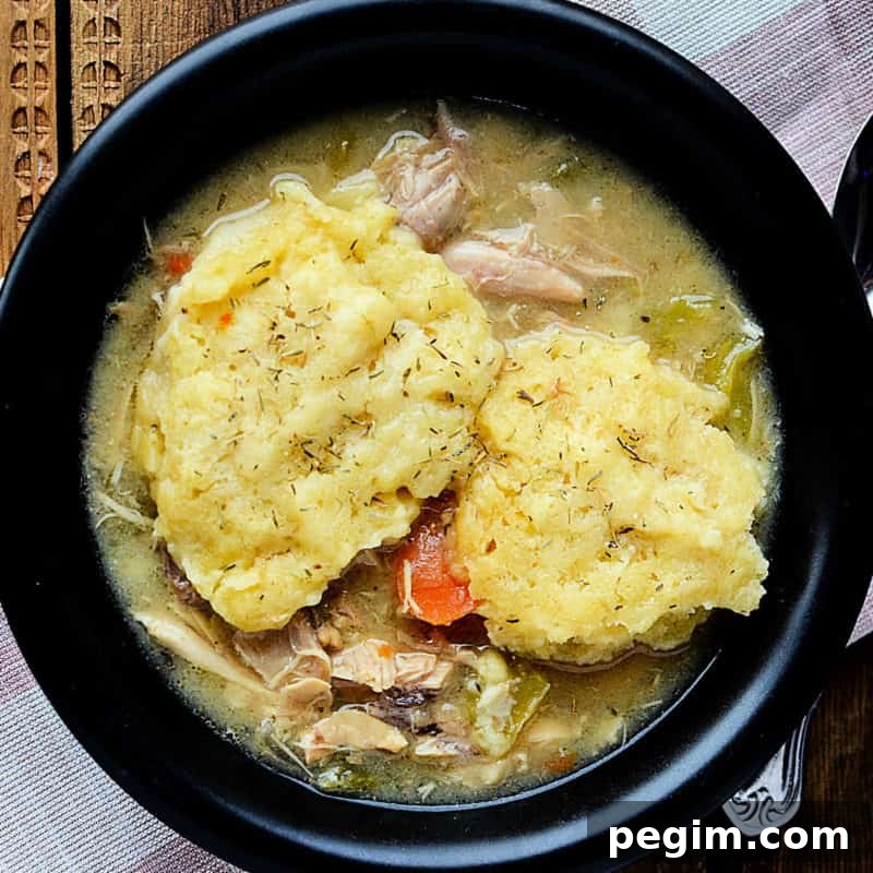 Crockpot chicken and dumplings in a dark bowl next to a spoon