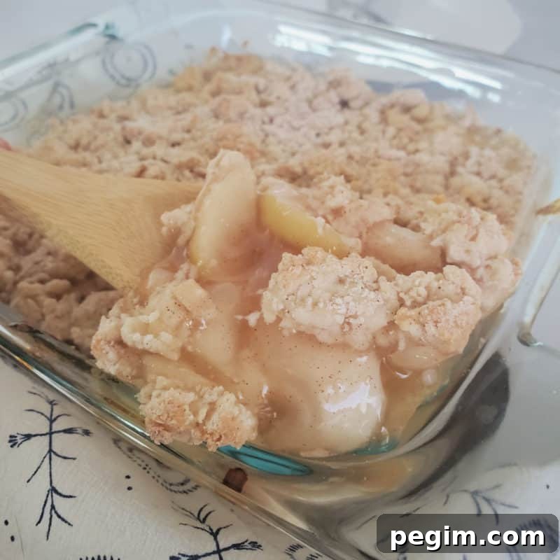 Bisquick Apple Cobbler in a glass baking dish with a wooden spoon scooping out some cobbler