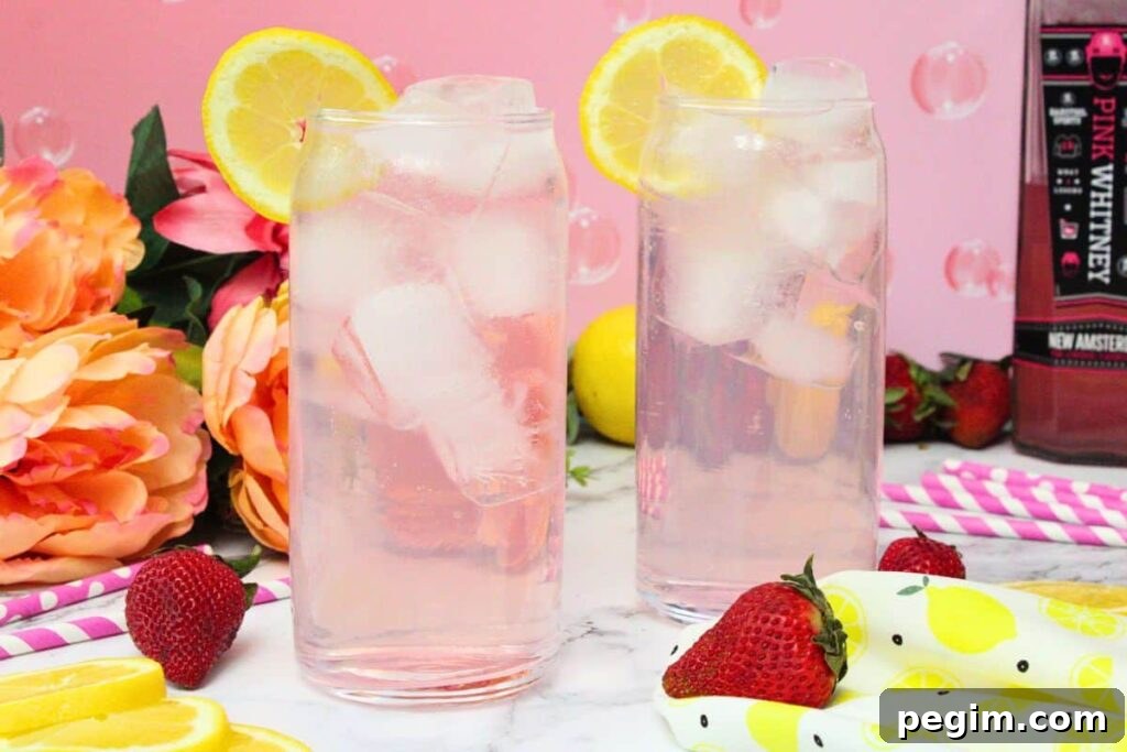 two pink whitney and sprite cocktails in tall glasses with a lemon slice in front of a pink background
