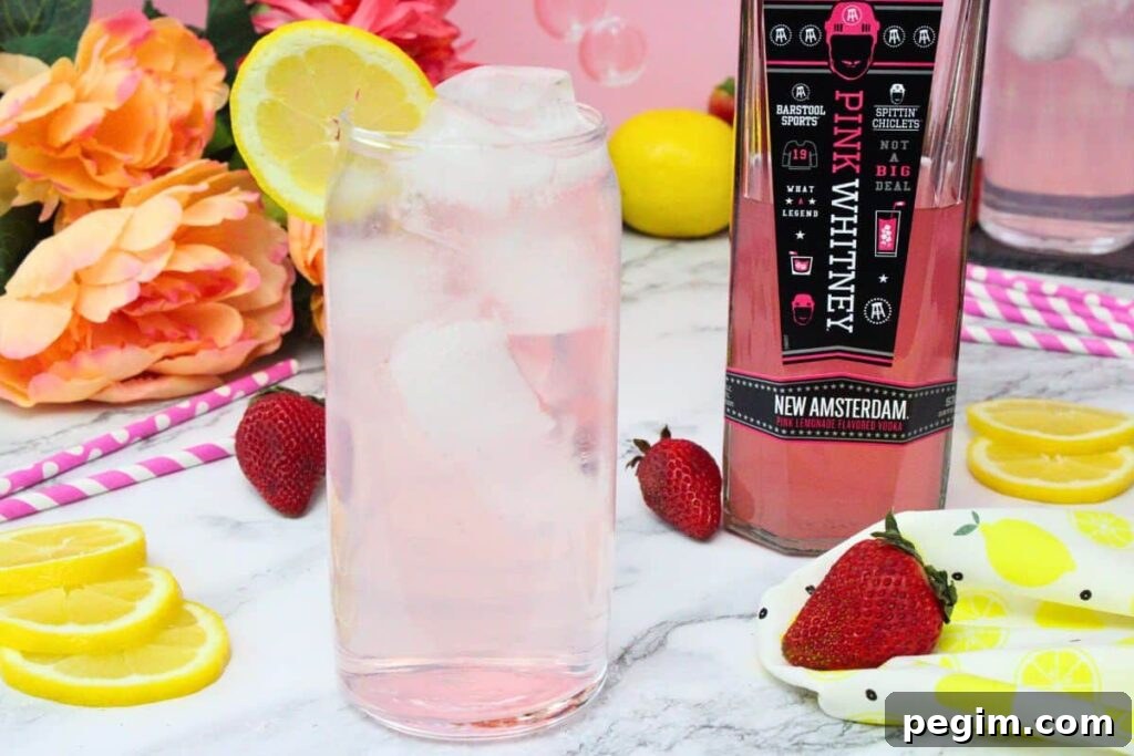 tall glass of pink whitney and sprite garnished with lemon next to pink whitney bottle