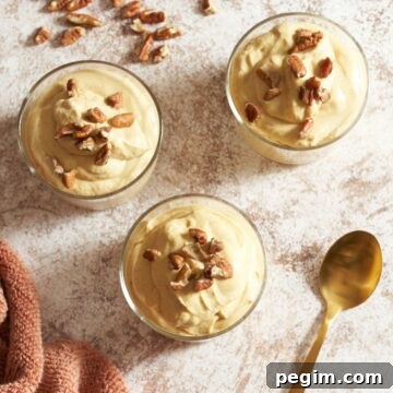 Three glasses filled with pumpkin mousse and topped with chopped pecans, a gold spoon is in the bottom right, more pecans are in the upper left.