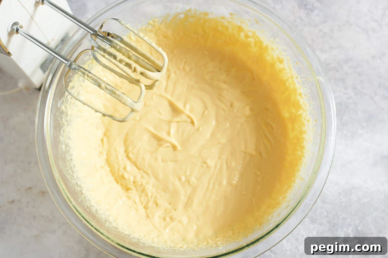 A hand mixer over a bowl containing mango pulp that has been blended with mascarpone cheese and sugar.