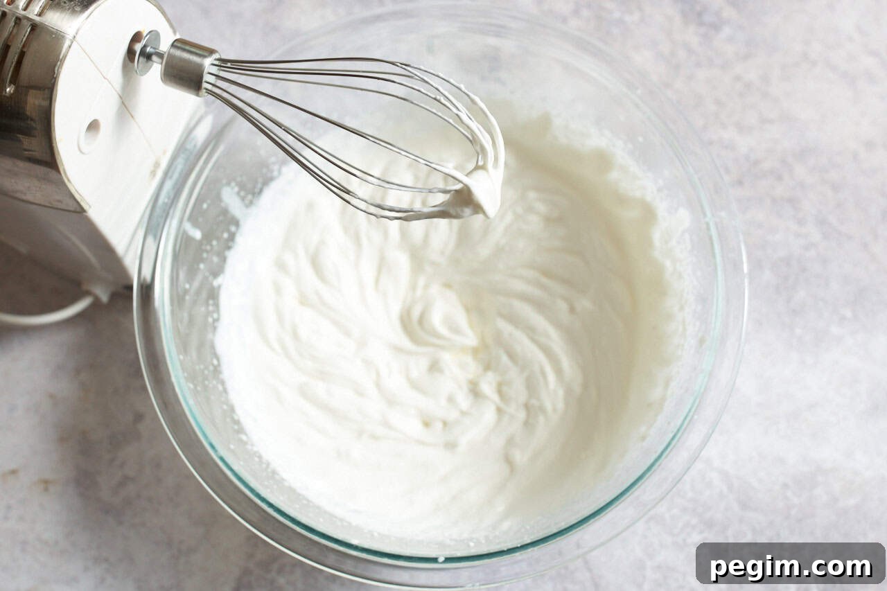A hand mixer with a whisk attachment over a bowl of whipped cream.
