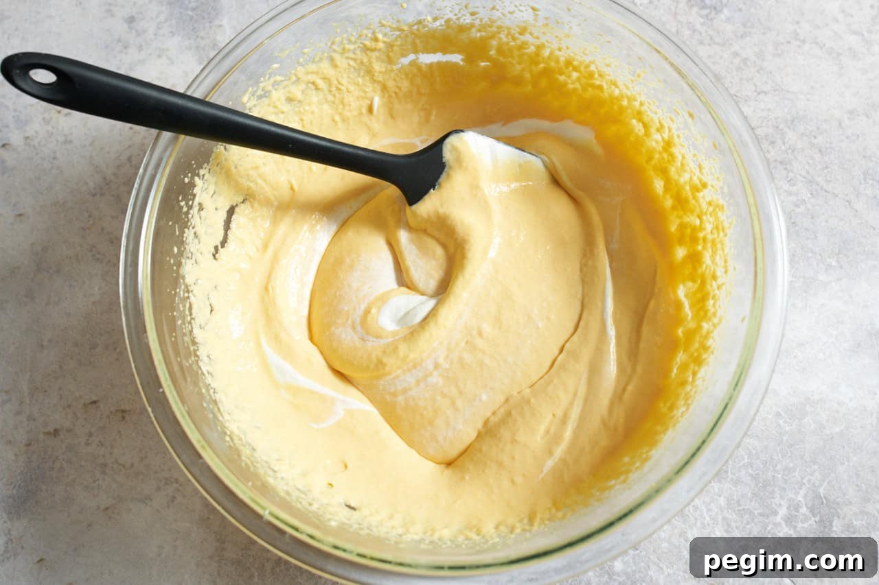 A large bowl with whipped cream being folded into a creamy mango mixture.