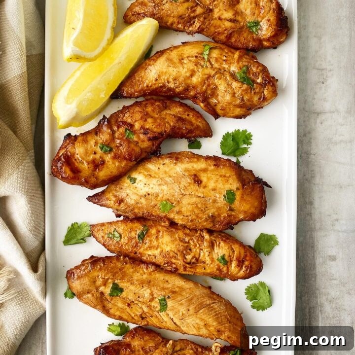 spicy naked chicken tenders topped with green cilantro on a white plate with lemon wedges