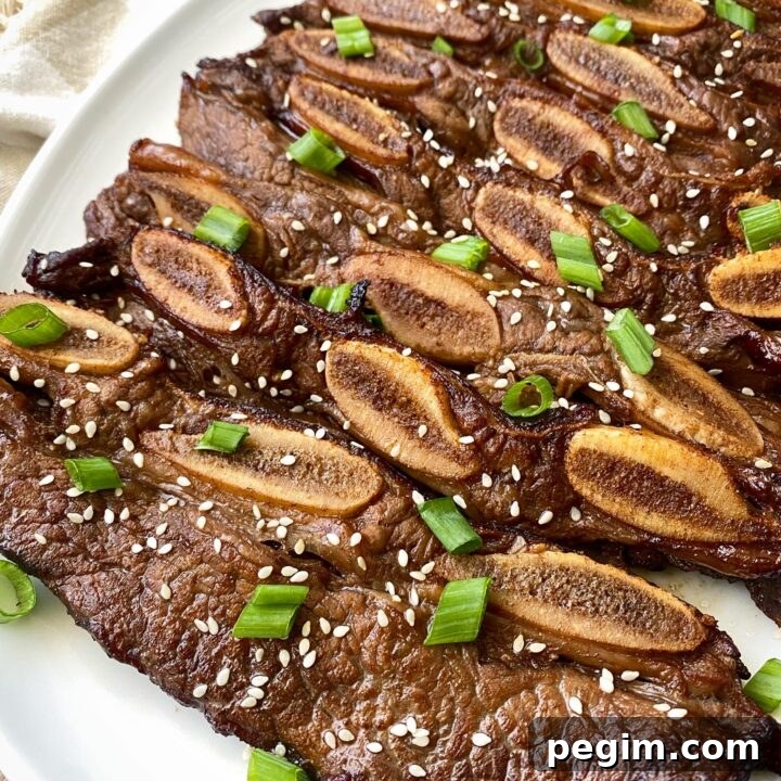 close up shot of cooked kalbi short ribs on a white plate garnished with sesame seeds and green onions
