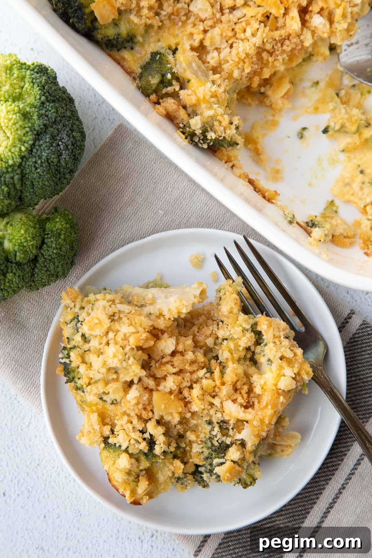 scoop of velveeta broccoli casserole on a small plate with a fork, next to a whole casserole in a white dish.
