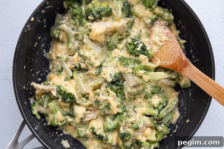 cheesy broccoli mixture in a large skillet with a wooden spoon.
