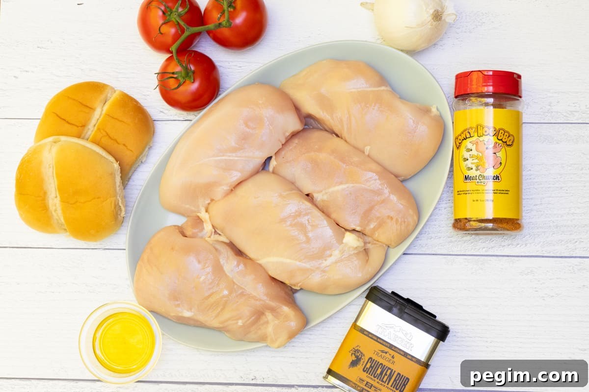 Chicken breasts raw on platter with tomatoes, buns, onion, olive oil, and seasoning surrounding plate.