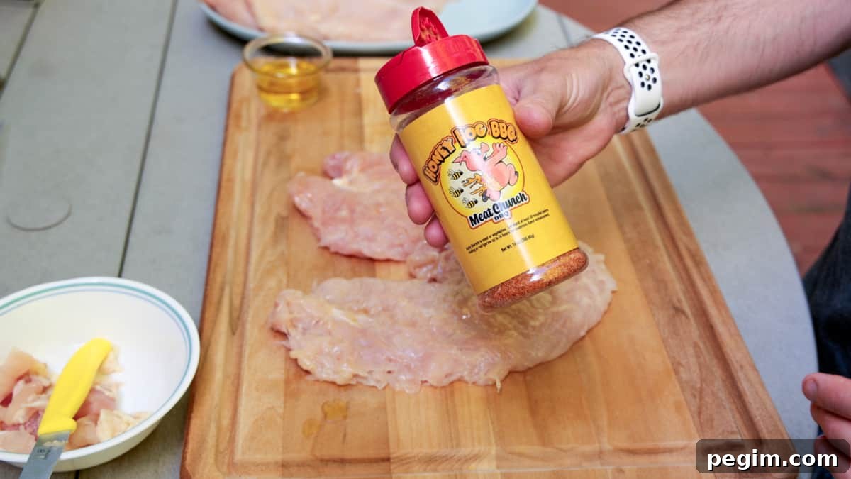 Chicken breasts on cutting board with a hand holding meat church brand seasoning in bottle.
