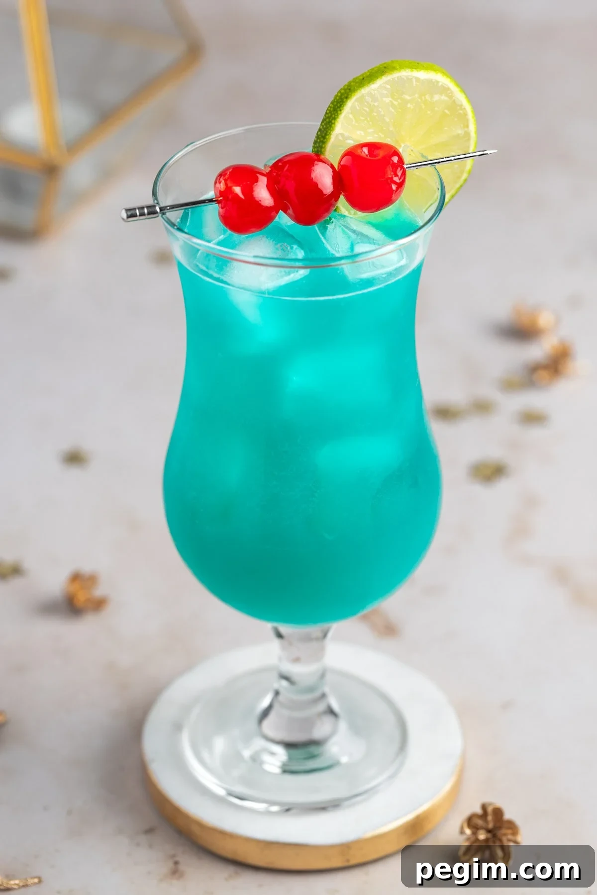 A tall hurricane glass filled with blue liquid and ice. Garnished with three maraschino cherries on a skewer and a lime wheel.