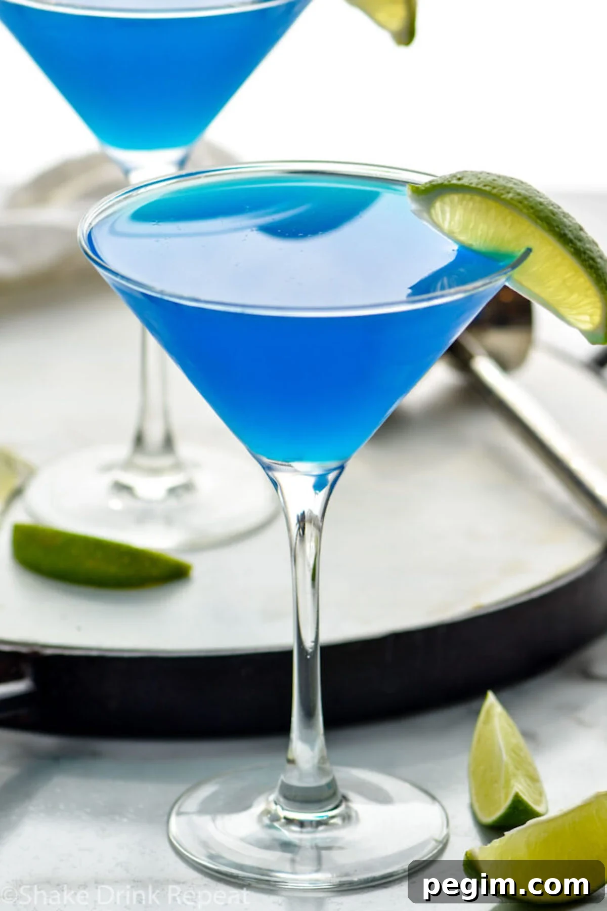 A bright blue daiquiri in a clear daiquiri glass garnished with a lime wedge.