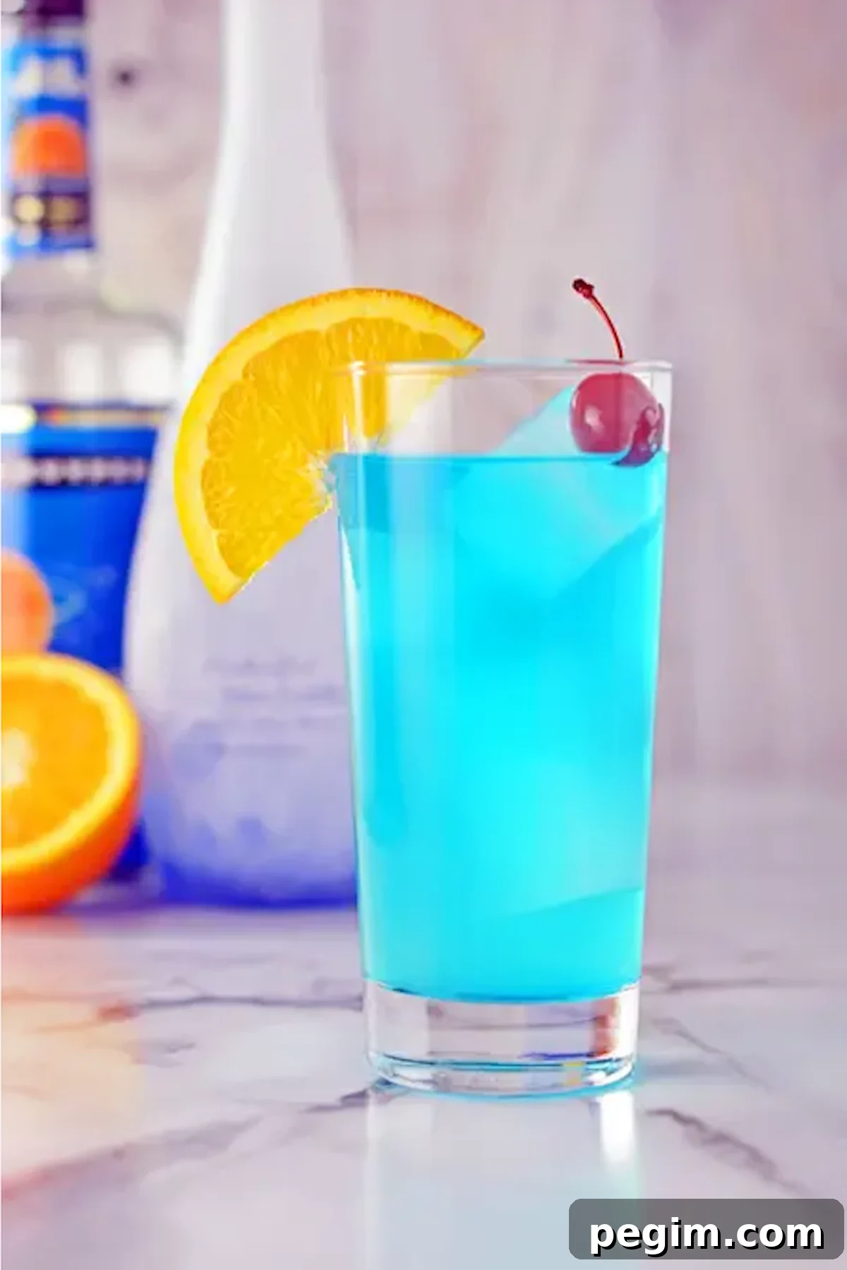 A neon blue cocktail on the rocks in a tall glass. Garnished with an orange slice and a maraschino cherry.