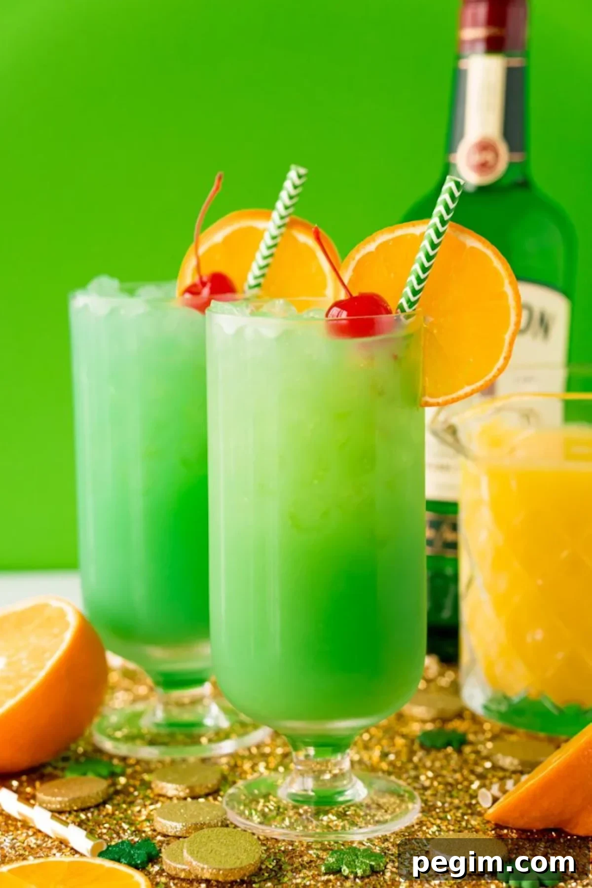 Two tall glasses filled with green drunken leprechaun cocktails each garnished with an orange wheel and a maraschino cherry.