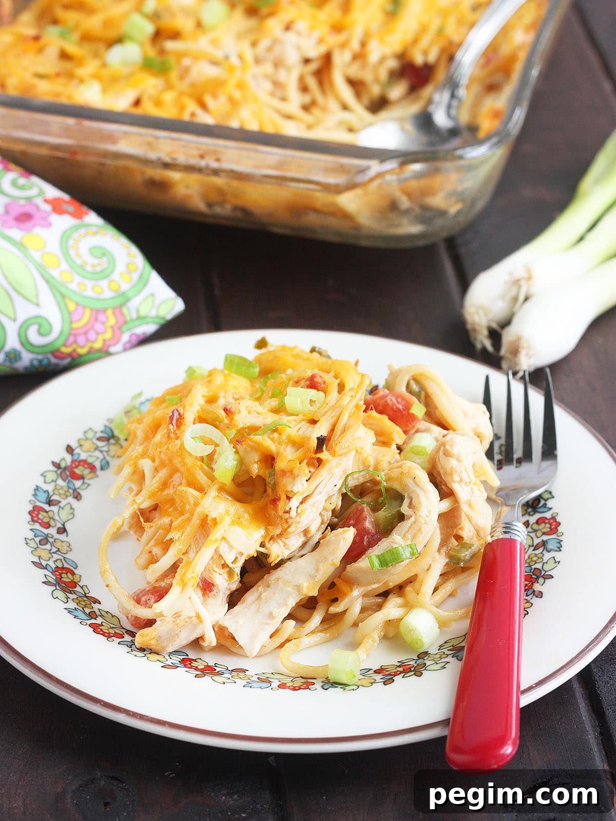 serving of cooked chicken spaghetti with rotel on a plate with a fork and a casserole dish in the background