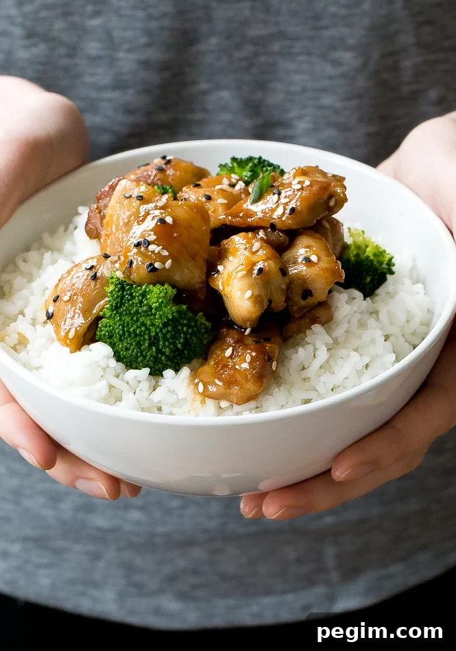 Hands holding white bowl with chicken, broccoli, and white rice