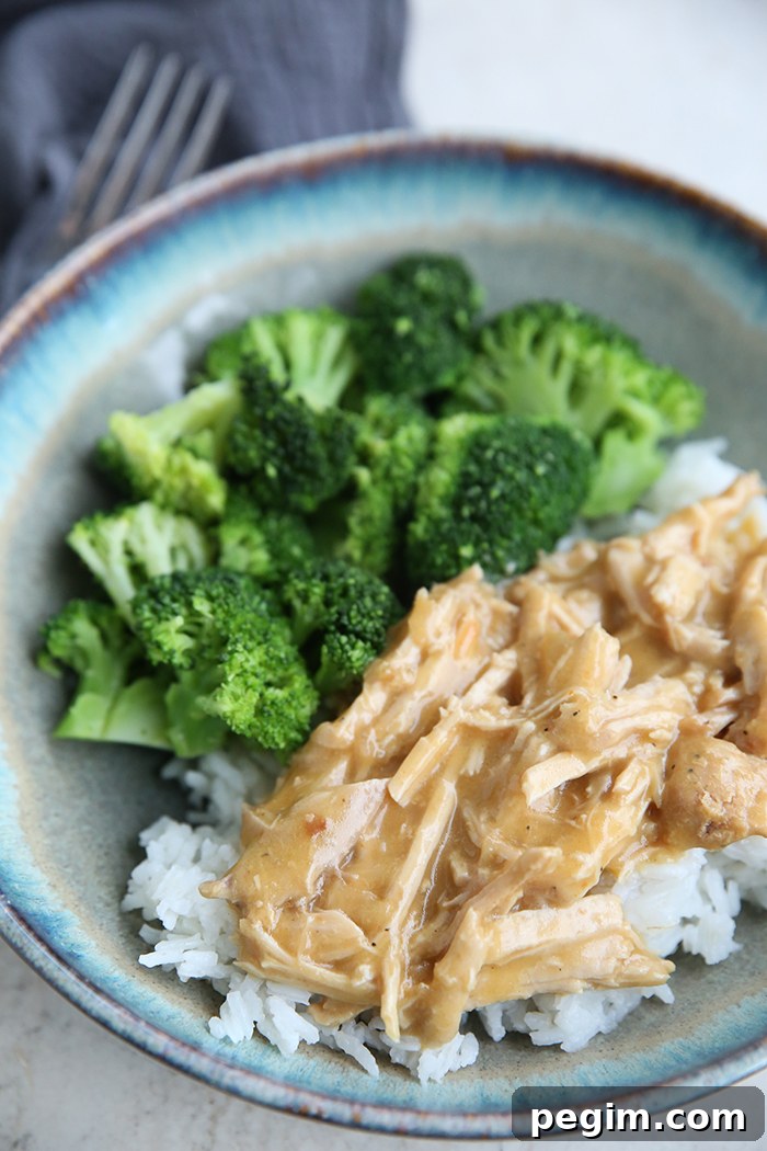 A dinner plate with pork roast and gravy over rice with a serving of steamed broccoli. A dark gray napkin and a fork head is at the top left of the plate.