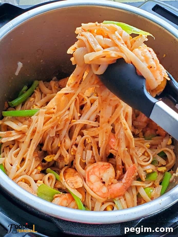 Instant Pot Pad Thai with chicken and shrimps in the instant pot being lifted with tongs