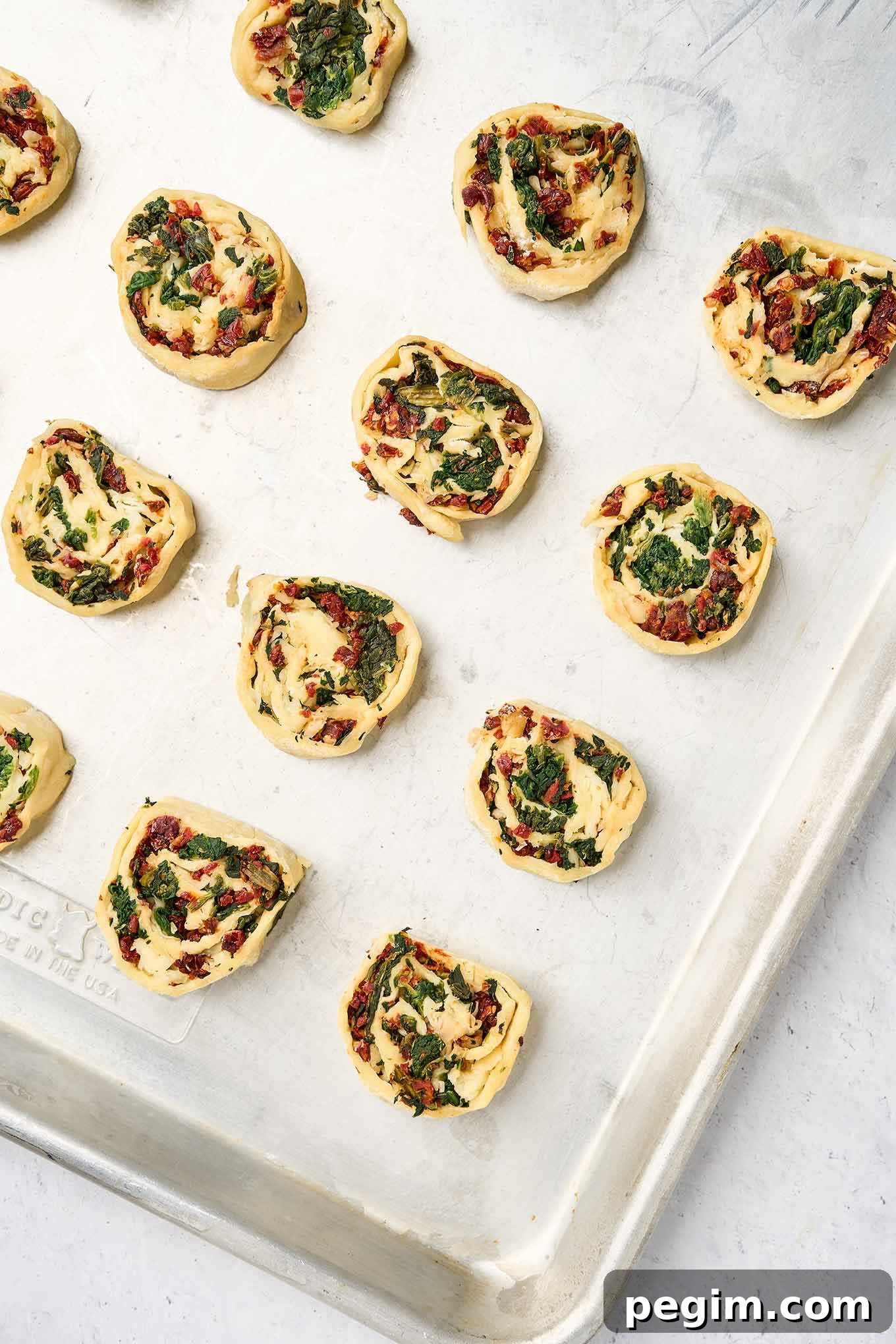 Sliced spinach pinwheel rounds arranged on a baking sheet, ready to bake.