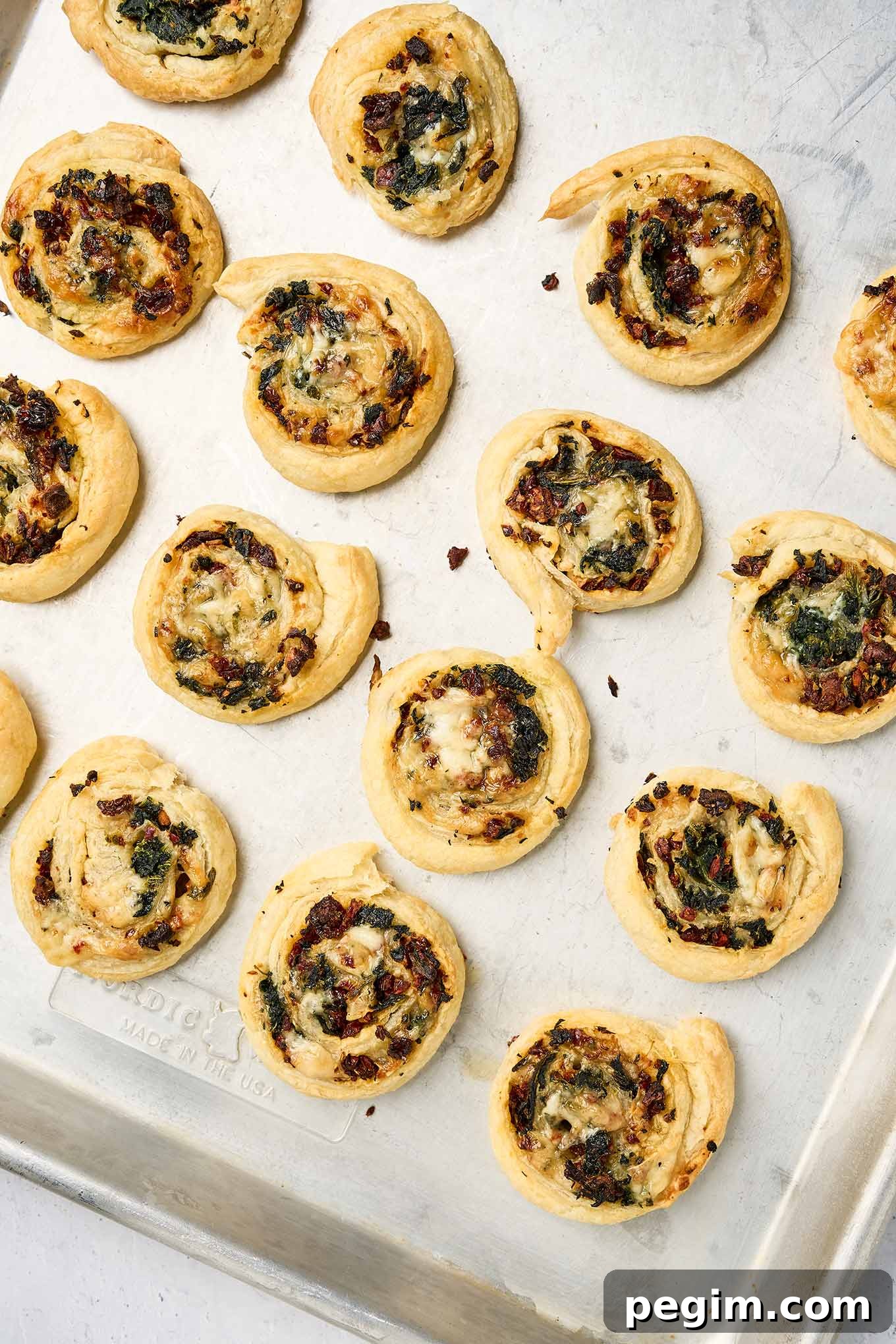 Spinach pinwheels fresh from the oven on a baking sheet, with crisp pastry and melted fontina cheese.