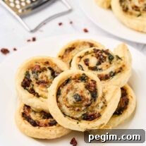 Golden spinach pinwheels made with puff pastry, spinach, fontina cheese, and sun-dried tomatoes, stacked on a white plate.