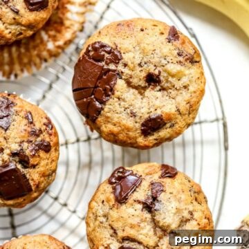 Banana muffins with chocolate chunks on a rack next to some bananas.