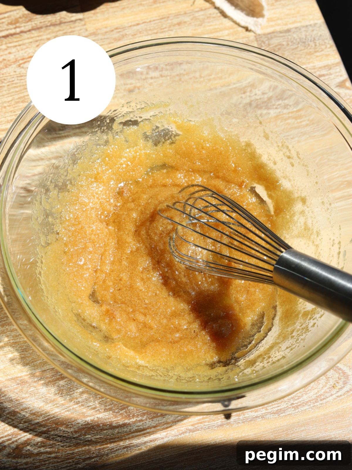 A glass bowl with brown sugar and butter and a wire whisk. 