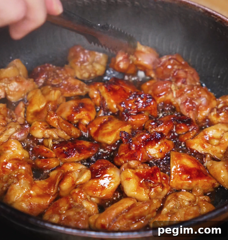 Chicken thighs cook in a skillet, bubbling in a thick soy and honey glaze. The pieces are browning evenly with a caramelized coating, indicating rich umami flavor development.