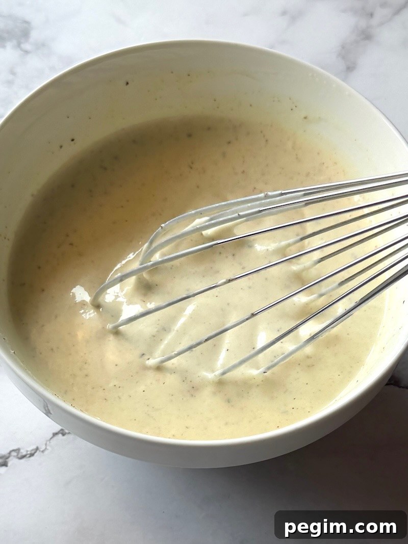 Dressing ingredients combined in a bowl with a whisk.