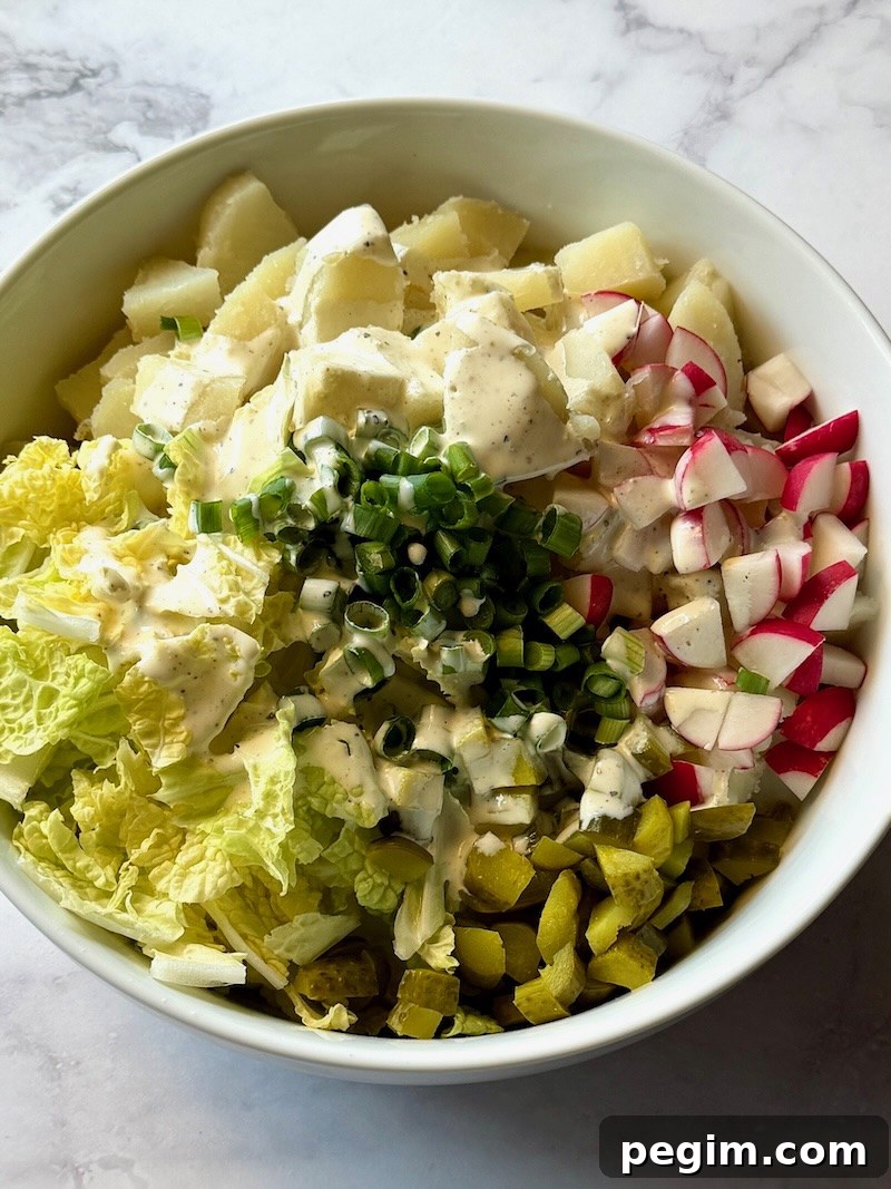 Potatoes in a bowl with cabbage, radishes, pickles, green onions, and dressing for Irish potato salad.