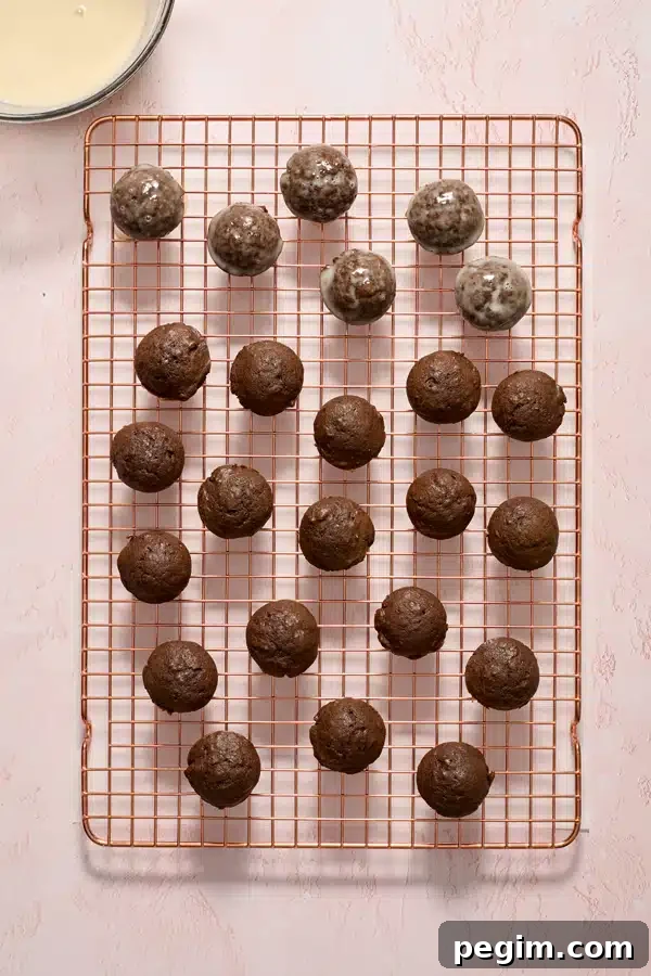 Chocolate donut holes on a wire rack partially dipped in glaze.