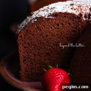 Chocolate chiffon cake sliced with whole strawberries placed on and in front of a dark purple ceramic plate on a black background.